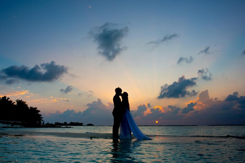 A couple shares a romantic moment on a tropical beach during a beautiful sunset, symbolizing love and serenity.
